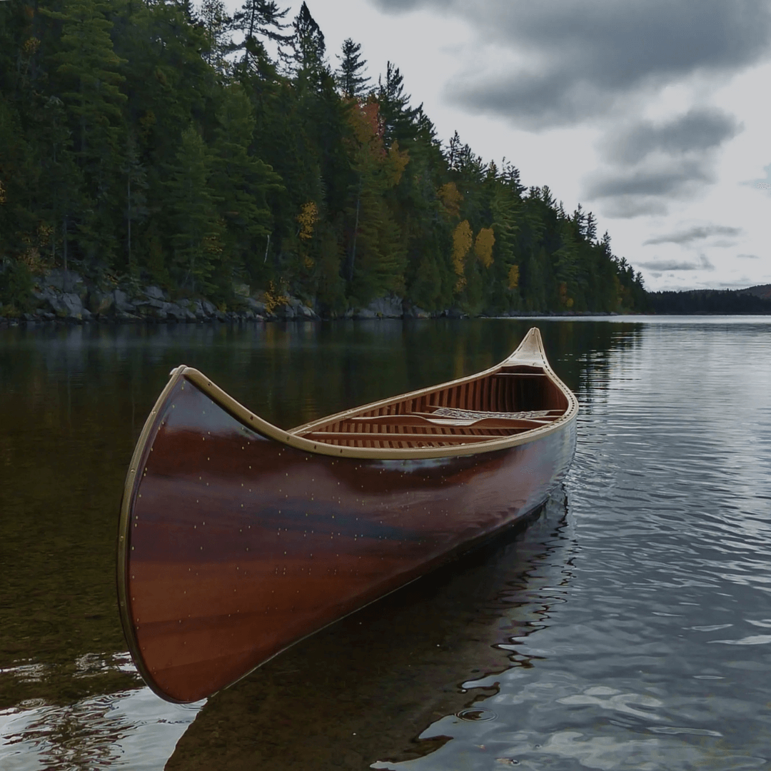 Beautifully crafted wooden composite canoe floating on a serene lake surrounded by lush forest, perfect for canoeing enthusiasts and those seeking a canoe for sale in Ottawa.